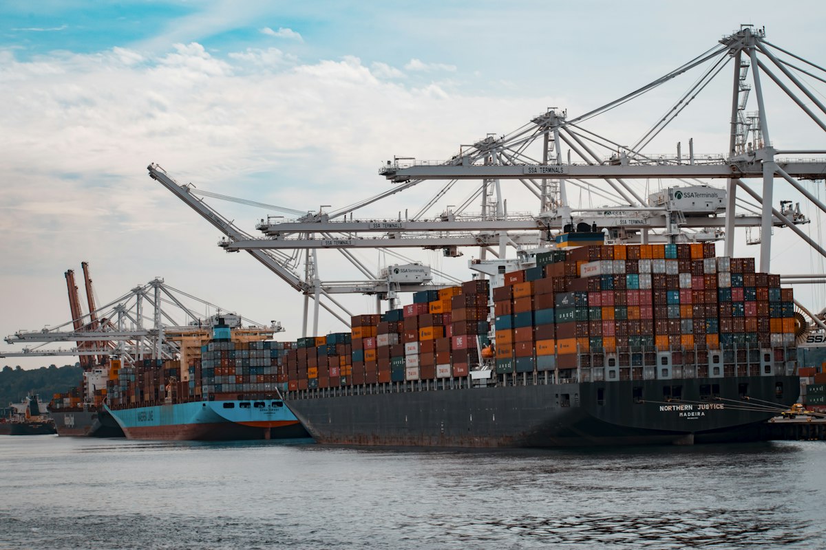 Aerial view of a container ship at a busy shipping port with cranes loading cargo