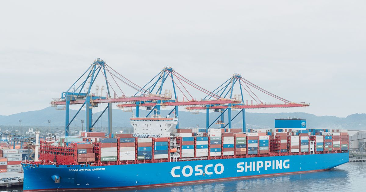 Large cargo ship docked at a busy shipping port with container cranes