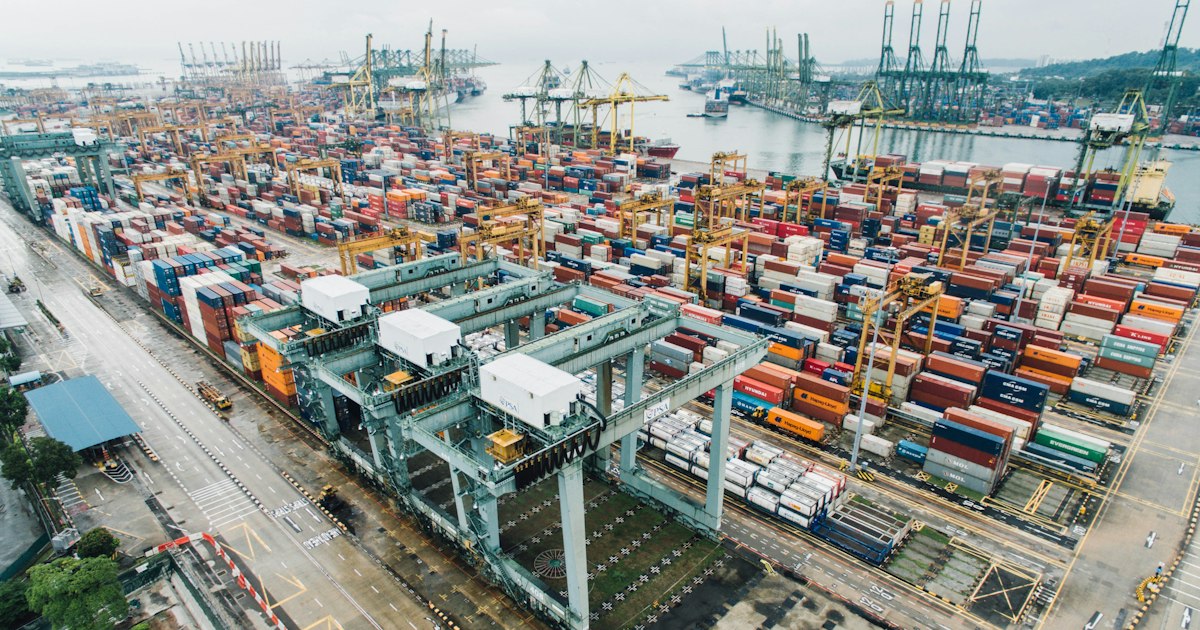 Colorful shipping containers stacked at a busy cargo port with loading cranes in the background